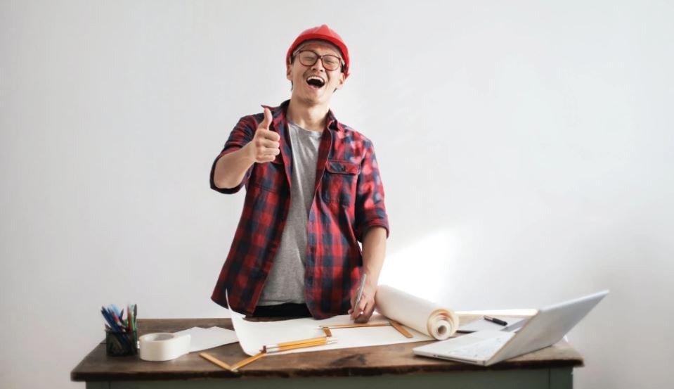 laughing-male-constructor-showing-thumb-up-at-working-desk