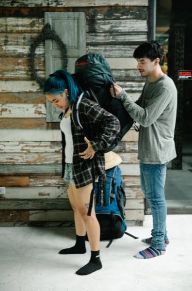 man-helping-woman-with-her-backpack